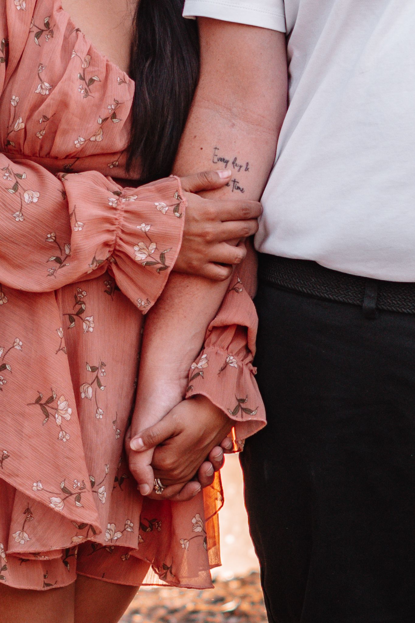 Close-up shot of couple holding hands while wearing pink floral dress and white shirt.