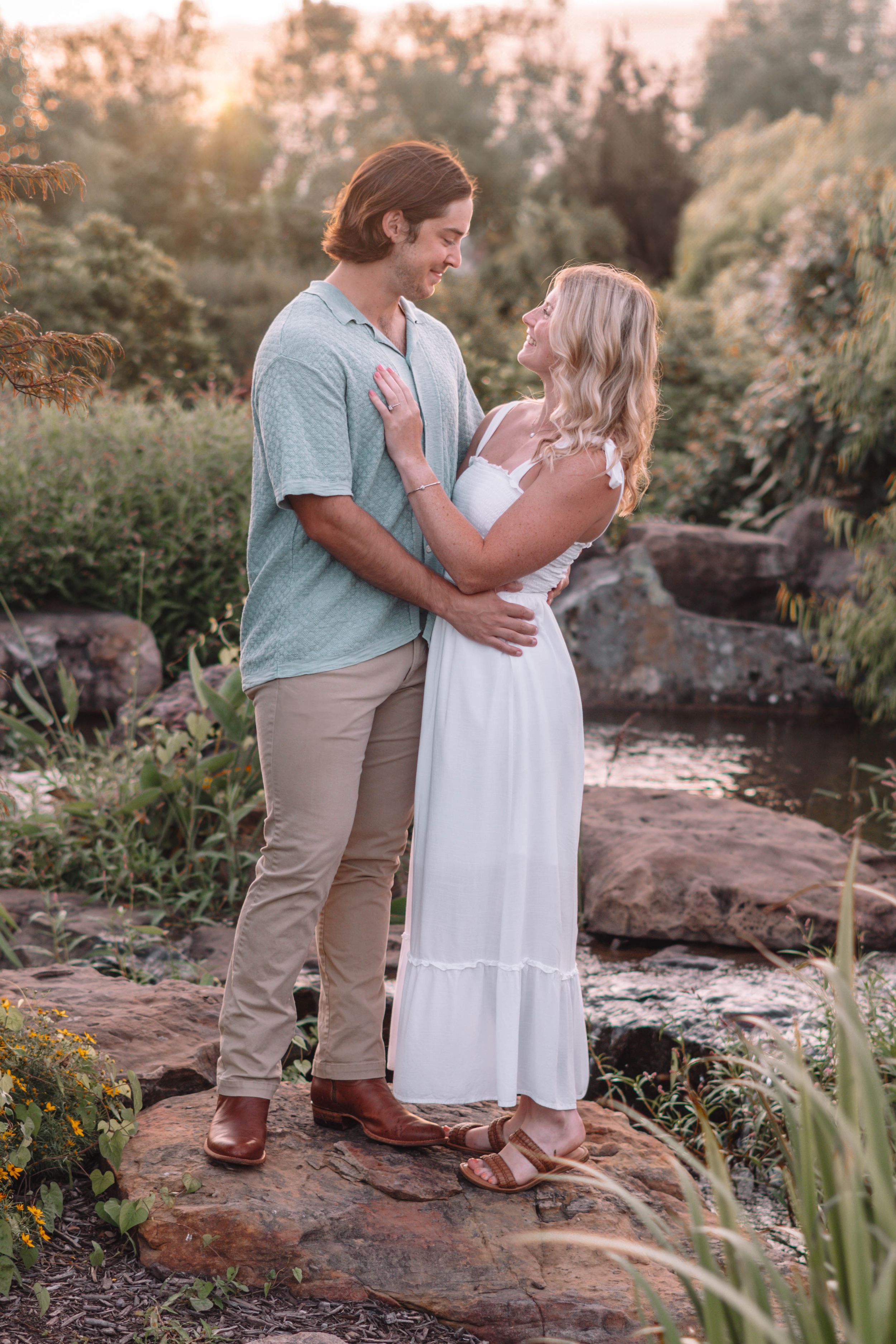 Couple stands together on rocky terrain during sunset photoshoot.