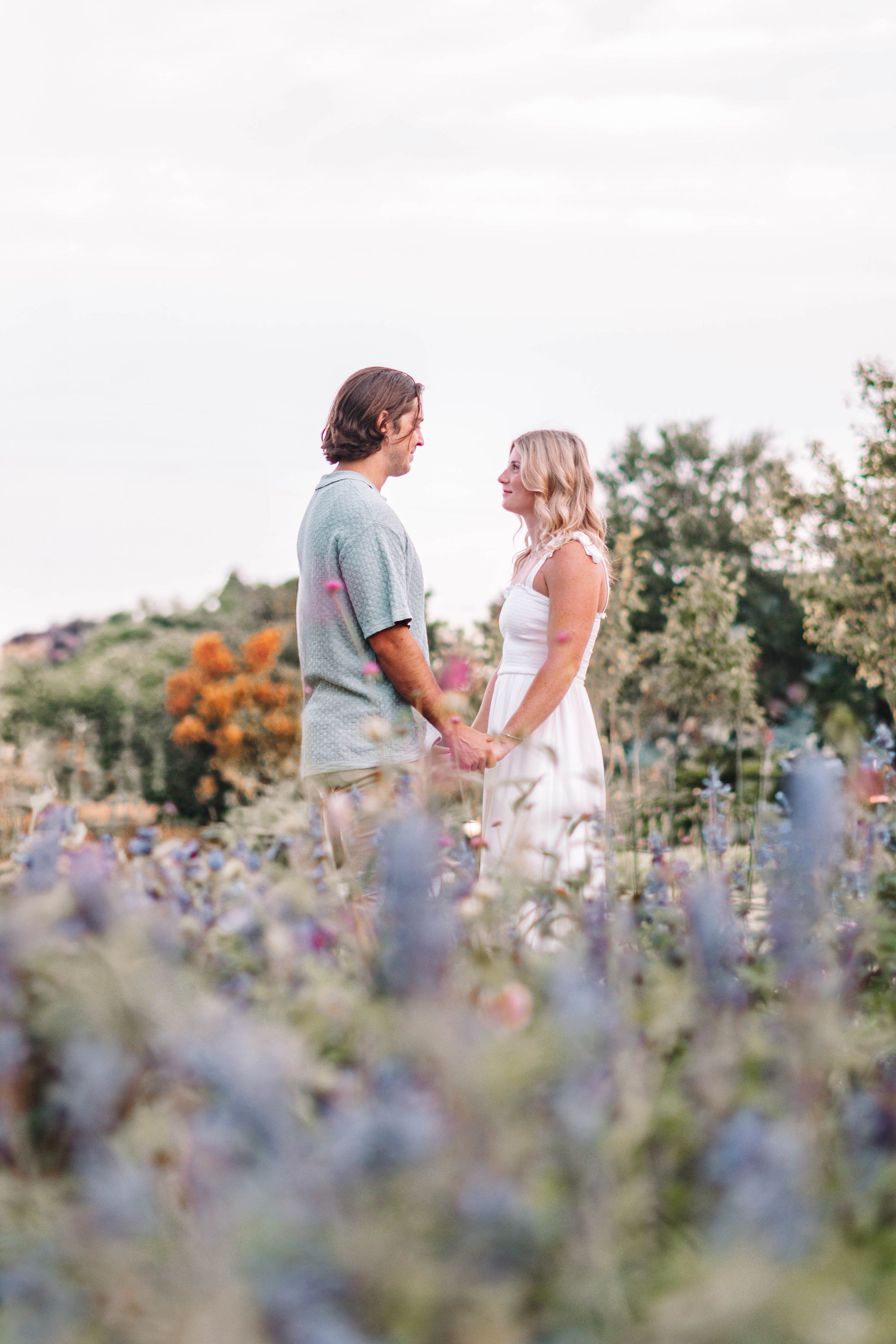 Couple shares intimate moment among purple wildflowers during sunset.
