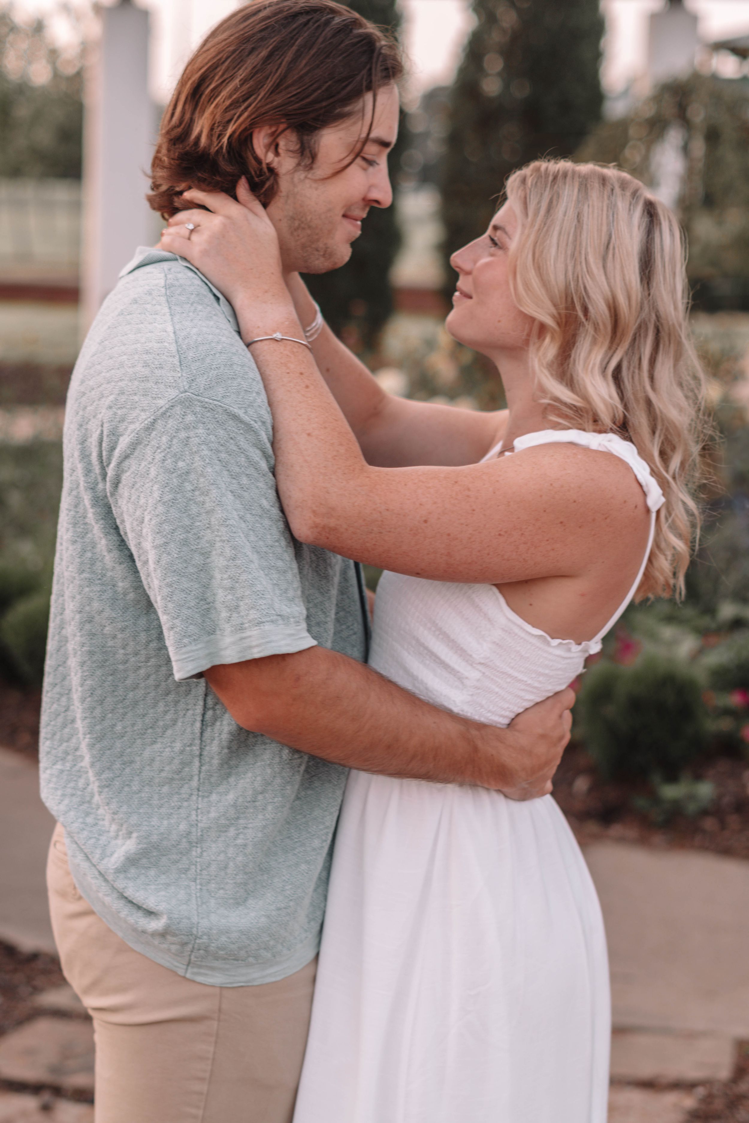 Tender embrace between couple wearing blue and white against sunset backdrop.