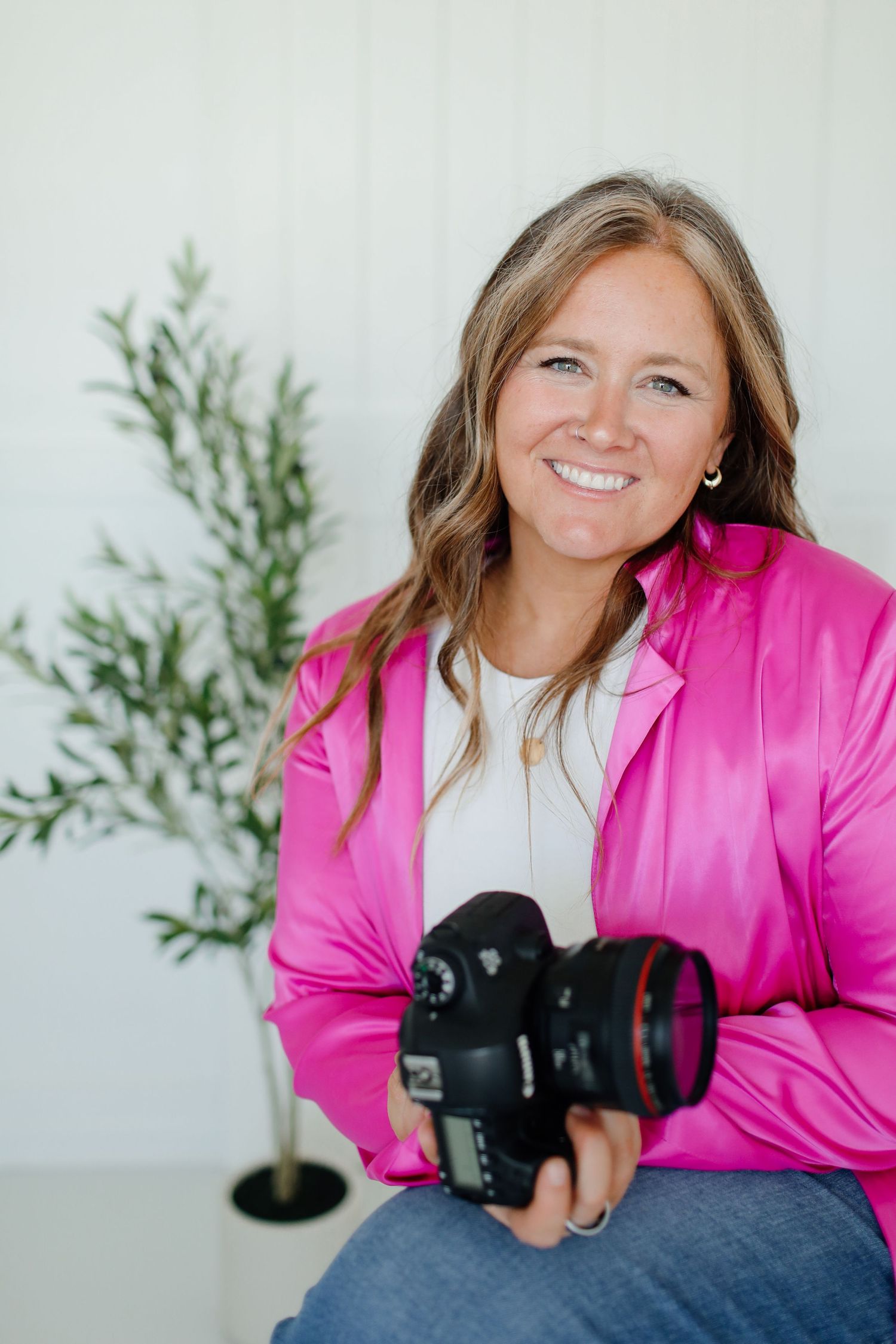 Professional photographer wearing bright pink blazer holding camera and smiling.