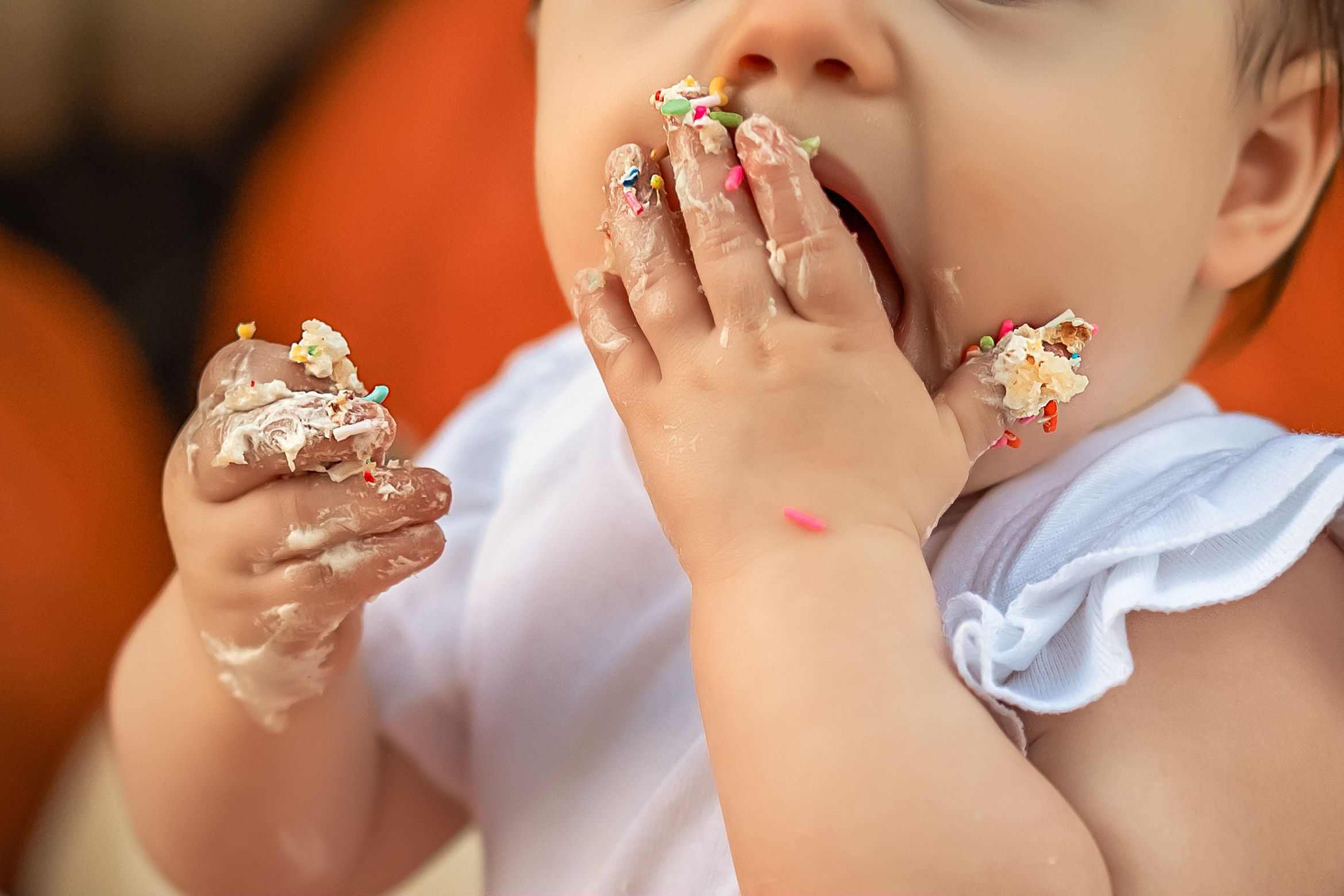 Baby girl takes messy bites of cake with frosting and sprinkles getting all over her face and hands with Alpharetta baby photographer.