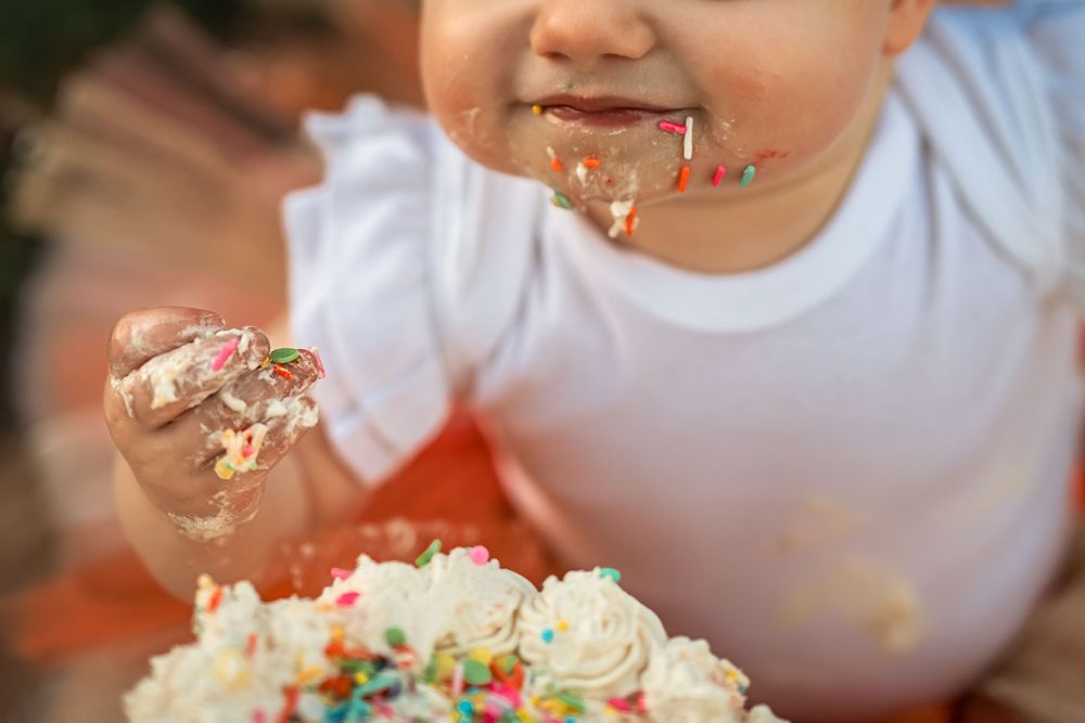 1-year-old girl covered in icing and sprinkles for pumpkin themed first birthday cake smash photo session.