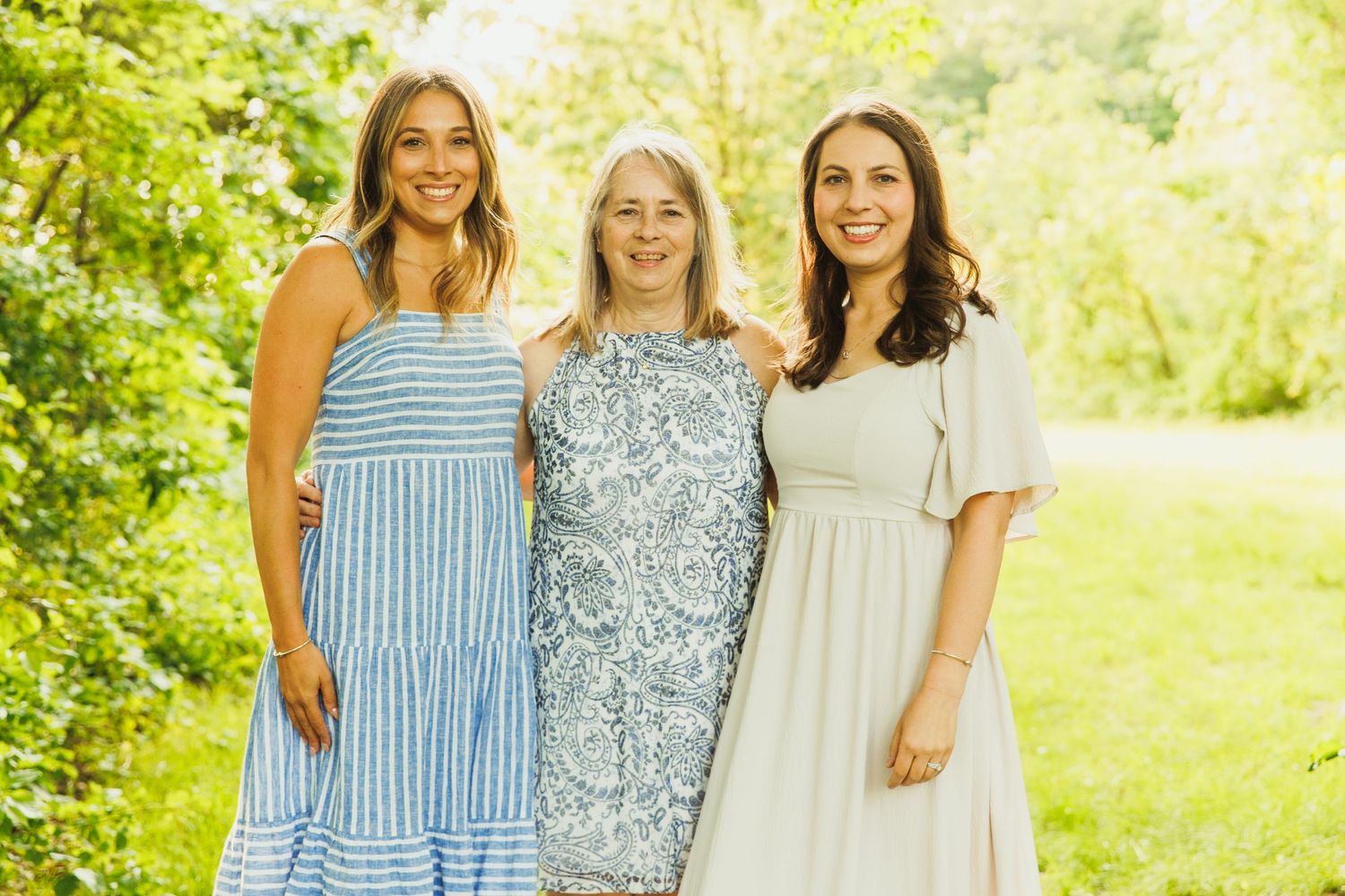 Three women in summer dresses pose together in garden setting.