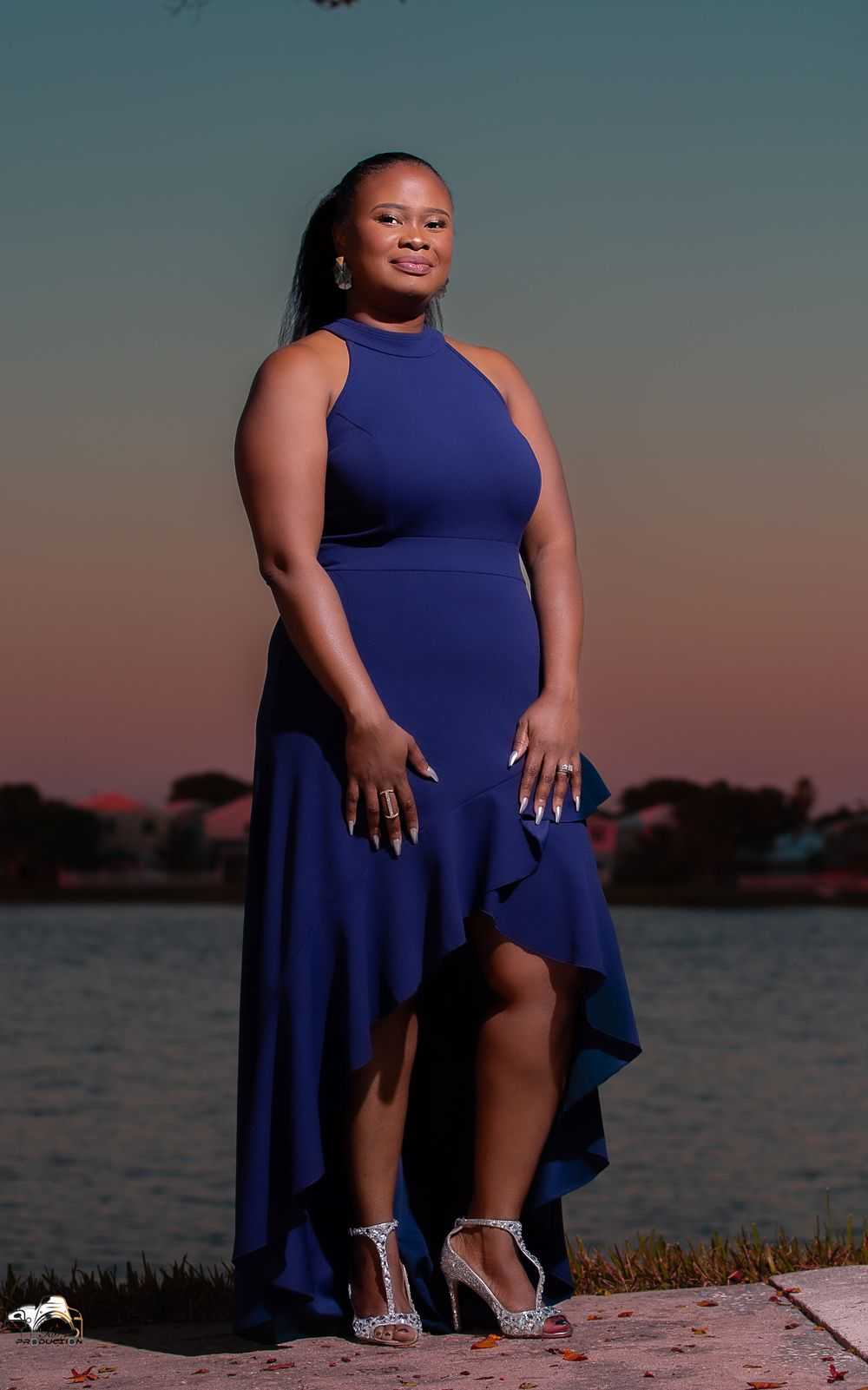 A person in a navy blue high-neck formal dress poses outdoors at sunset.