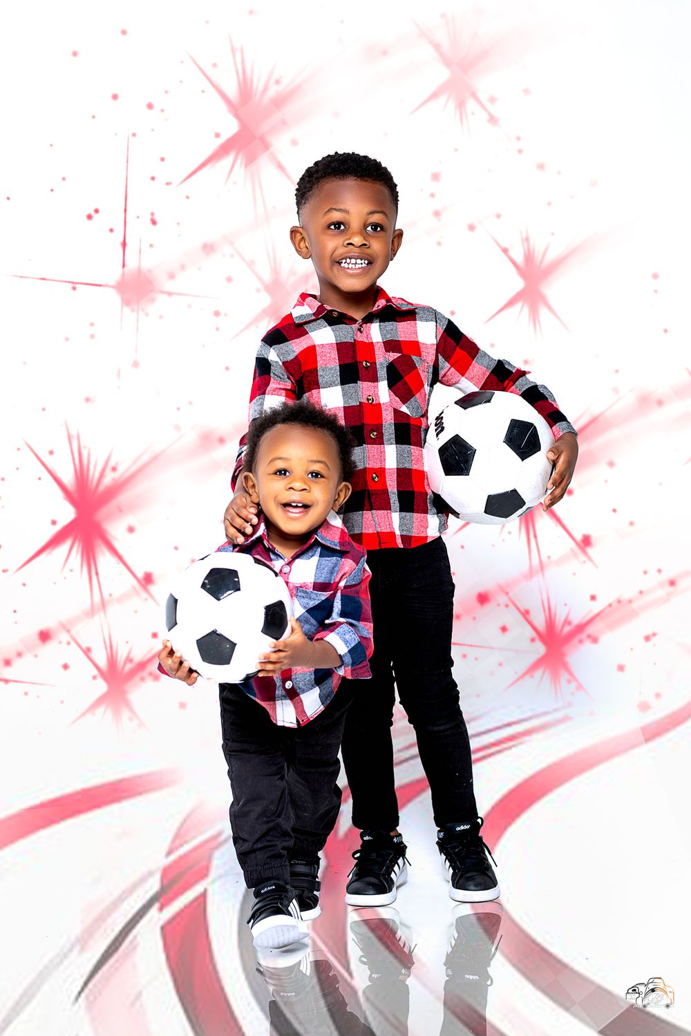 Two young ones posing with soccer balls in matching plaid shirts against pink starburst backdrop.