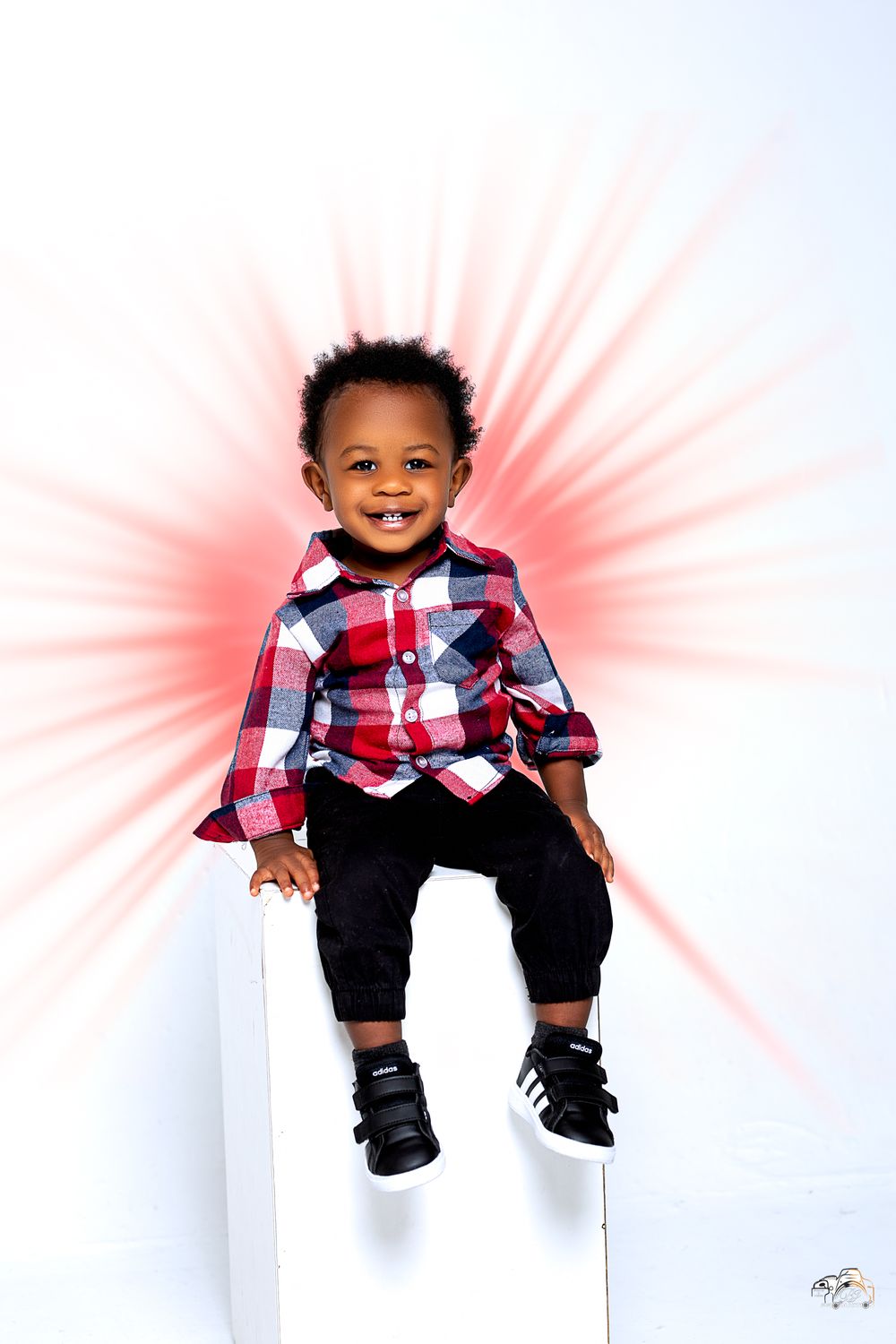 Happy child in plaid shirt sitting on white platform with red starburst background.