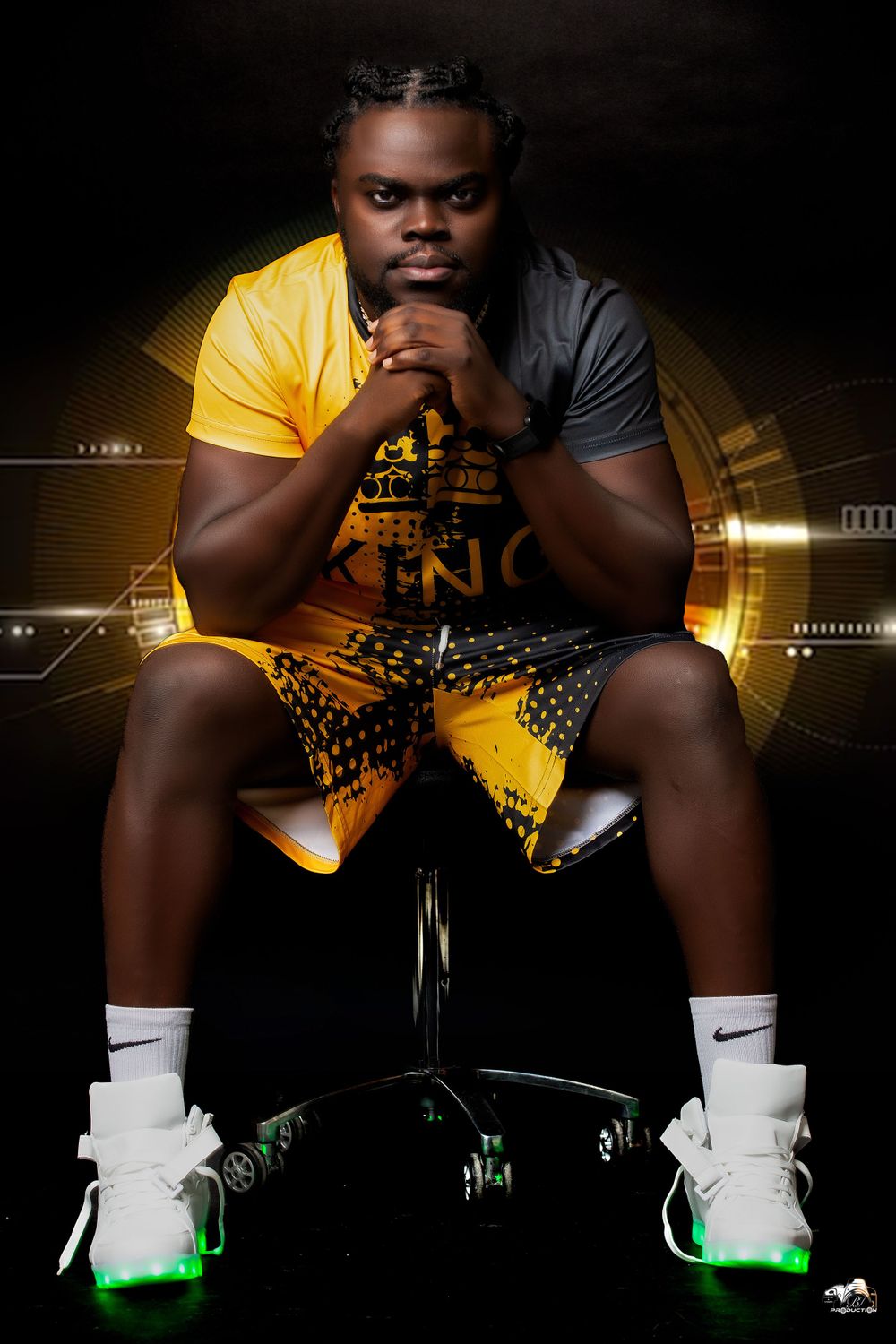 A person in yellow and black sportswear sits on a chair against a dark background with lighting effects.