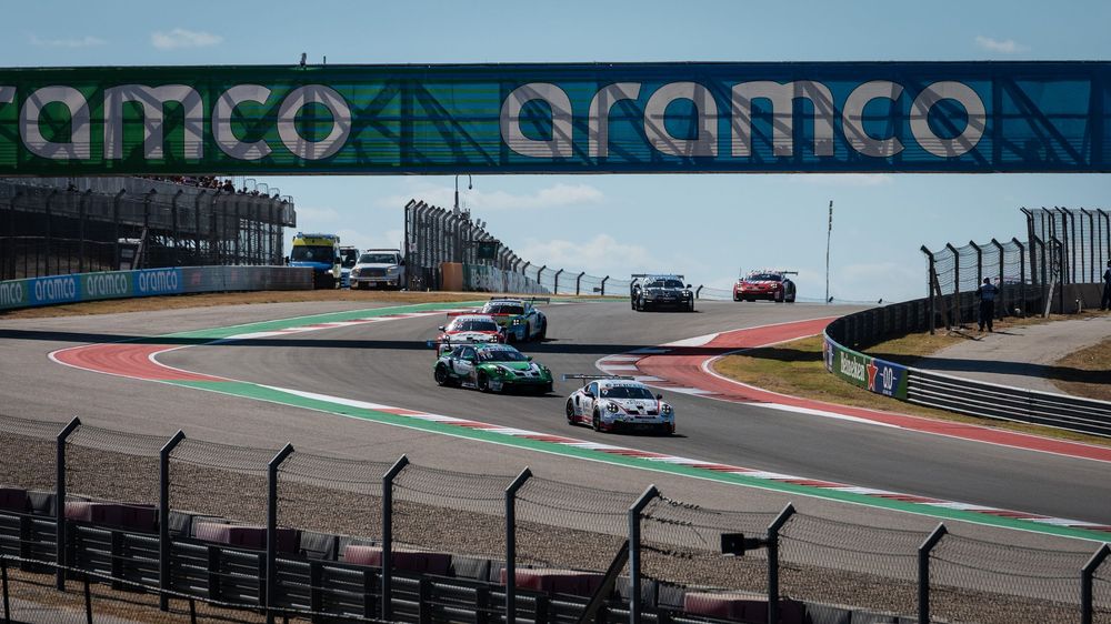 Racing cars compete on a circuit under an Aramco sponsorship bridge at a professional motorsport event.