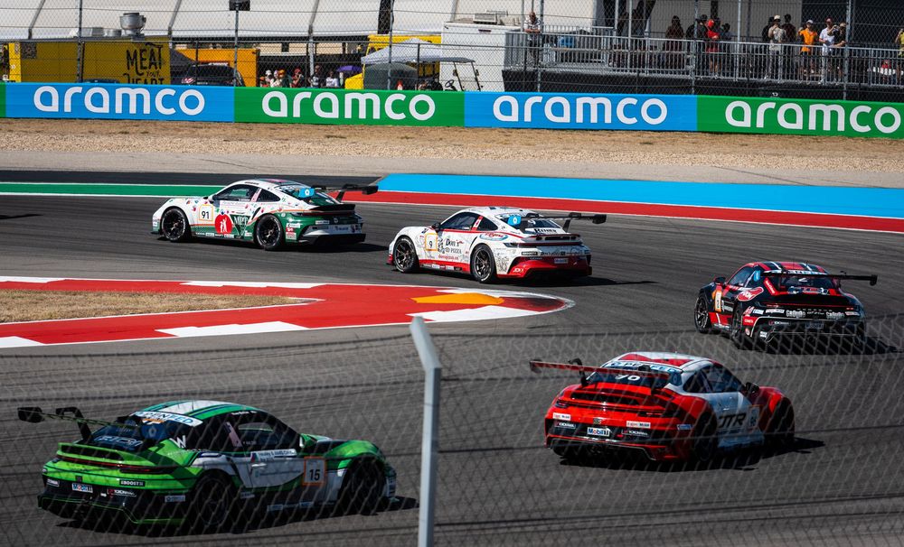 Multiple Porsche GT3 race cars compete on track at an Aramco-sponsored motorsport event.