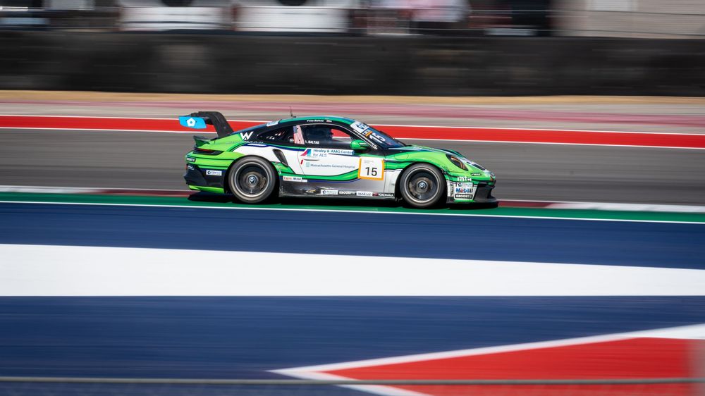 Green and white Porsche race car speeding on a circuit track during a professional motorsport racing event.