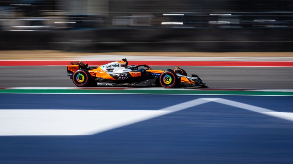 McLaren Formula 1 car racing on track in orange and black livery during a Grand Prix event.