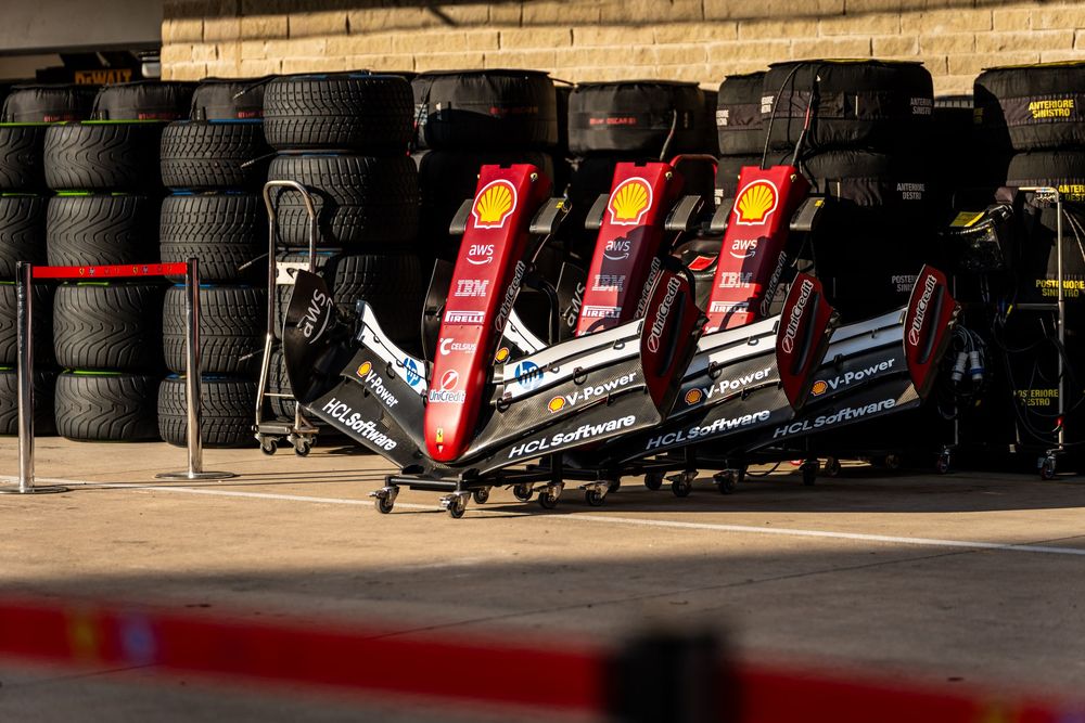 Ferrari F1 cars lined up in pit lane with Shell-branded nose cones and stacked tires in the background.