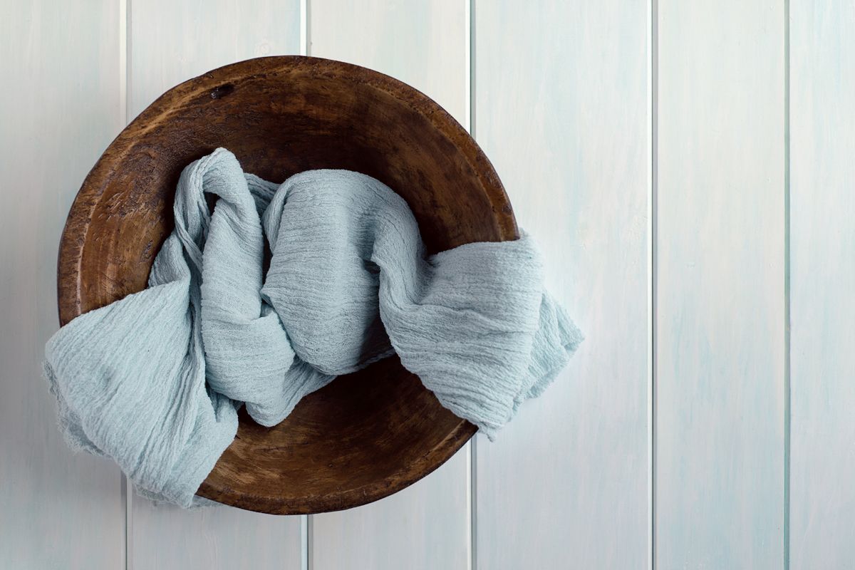 Top view of dark wooden newborn baby bowl prop in Baltimore Ontario with blue wrap draped over bowl on light blue wooden board backdrop.*