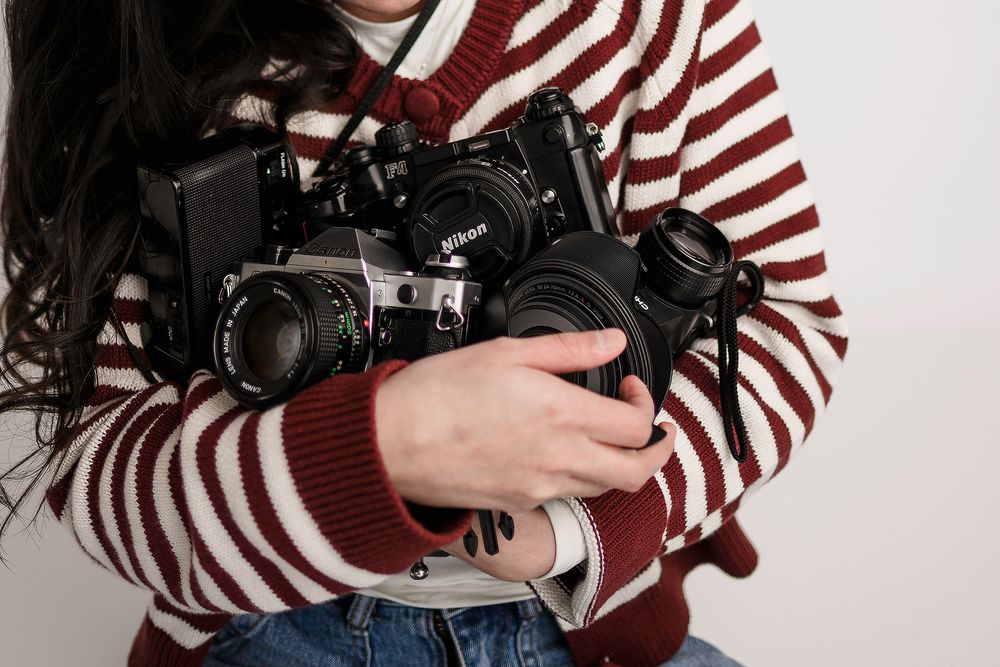 Woman in red striped sweater holding multiple vintage film cameras in her arms.