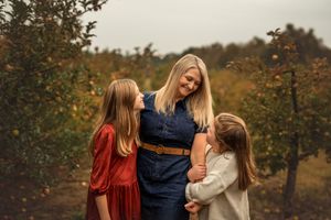 Two girls share loving looks with mom during an autumn outdoor portrait session in an apple orchard.