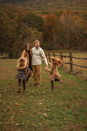 Family playing and walking together in a rustic field with wooden fencing during fall for family photos with Marietta photographer.