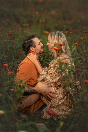 Husband and wife share intimate embrace in a wildflower field at sunset, with zinnias blooming around them.