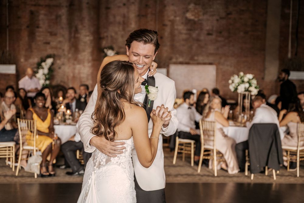 A wedding reception in a rustic brick venue with guests dancing and celebrating at tables.