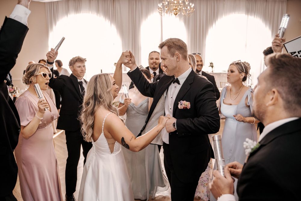 Wedding party dancing and celebrating together during reception in elegant ballroom with chandelier.