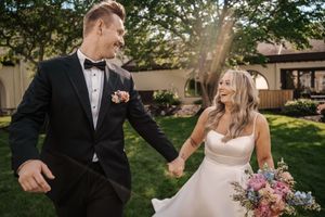 A couple in wedding attire dances and twirls in a lush garden setting during golden hour.