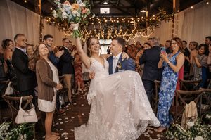Wedding guests dance and celebrate on a crowded dance floor under string lights at an evening reception.