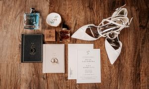 Wedding rings and invitations arranged on rustic wooden surface with white cords and decorative elements.