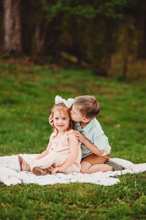 Children playing together on a white blanket in a grassy park setting.