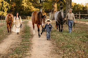 A group walks down a country path with three horses during golden hour at sunset.