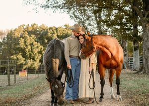 Two horses stand with their handlers in a fenced pasture at sunset.