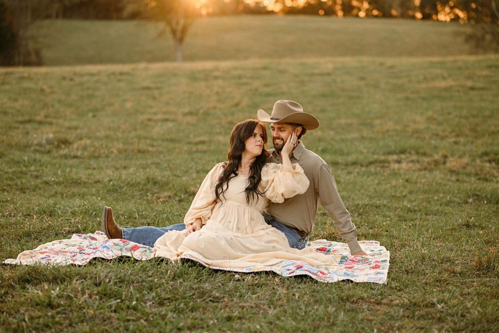 A romantic sunset picnic scene on a blanket in a rustic field.
