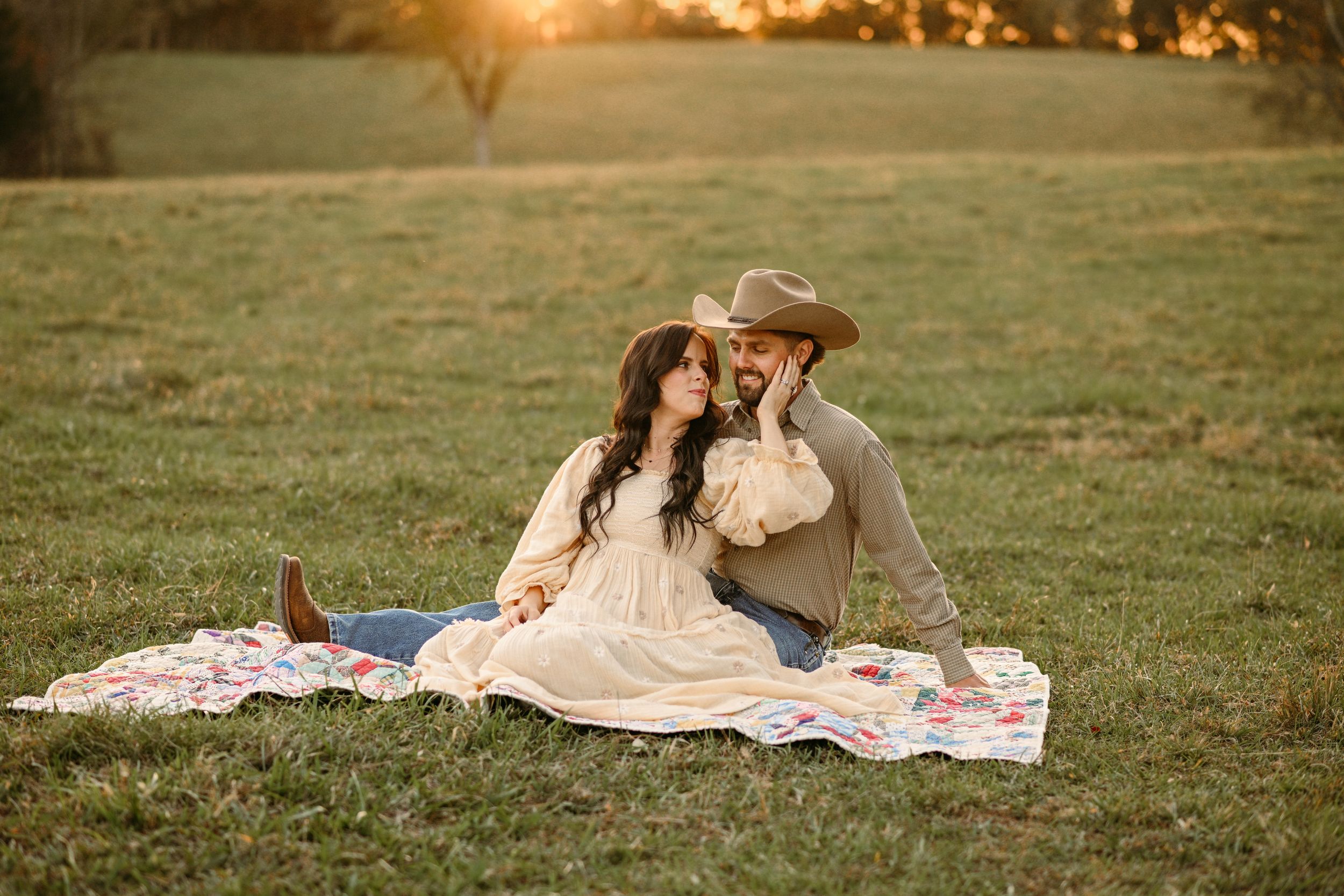 A romantic sunset picnic scene on a blanket in a rustic field.