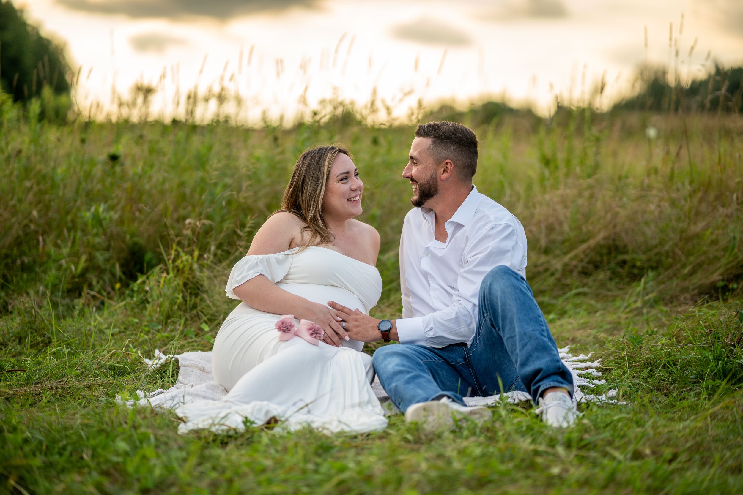 Romantic maternity photo session with couple sitting on blanket in golden summer field.