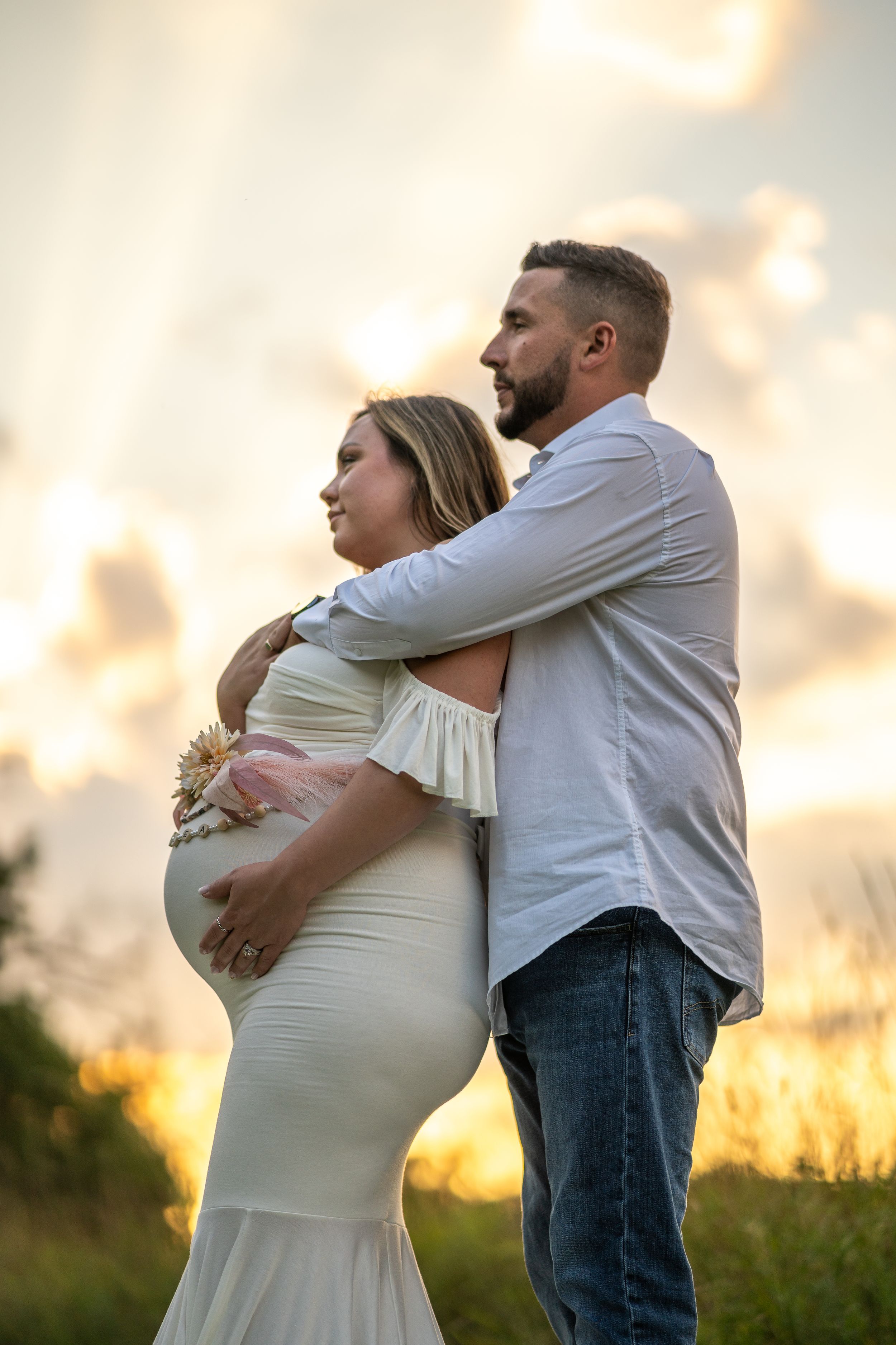 Silhouetted maternity portrait against dramatic sunset sky in tall grass field.