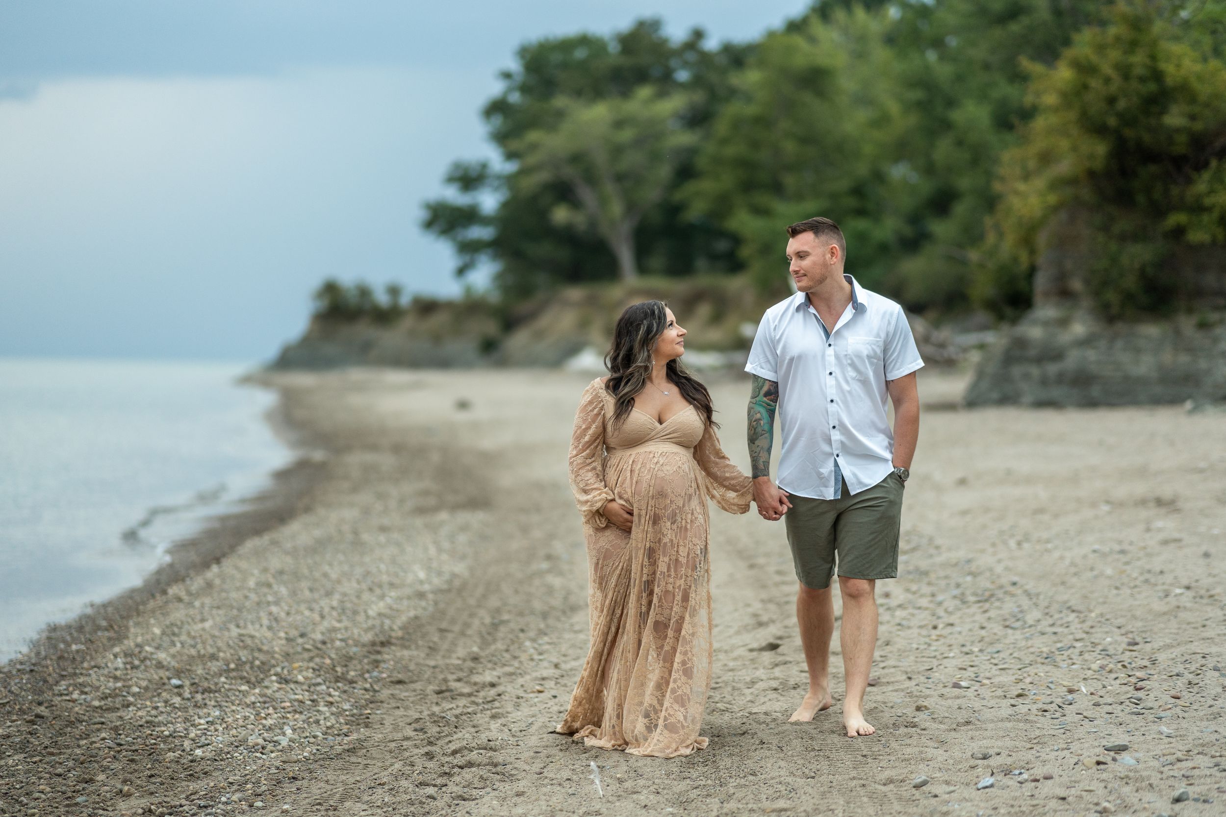 A couple strolls along a scenic beach shoreline wearing casual attire on an overcast day.