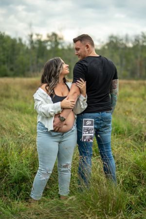 A couple sharing an intimate moment in a field while holding ultrasound photos.
