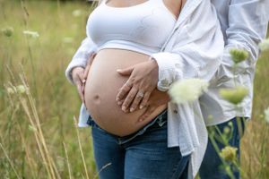 Close-up shot of a pregnant belly being lovingly cradled in a beautiful sunlit field.