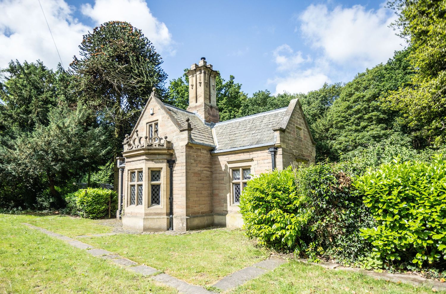 Stone Gothic cottage with pitched roof and decorative gables surrounded by trees.