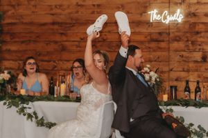 Newlyweds celebrate with raised shoes at rustic barn reception.