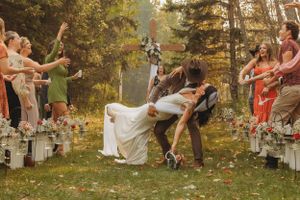 Wedding guests celebrate joyfully along an aisle lined with mason jar candles in a wooded outdoor setting.