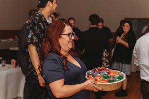 A guest carrying colorful appetizers on a wooden platter at a wedding reception.