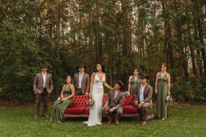 Wedding party poses with vintage red couch in forest setting.