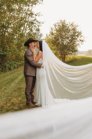 Couple shares intimate moment with flowing veil in outdoor wedding portrait.