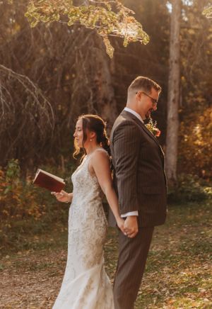 A wedding couple stands back to back in a rustic autumn forest setting.