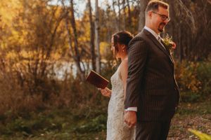 A couple shares a quiet moment during a fall wedding ceremony in the woods.