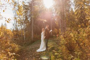 Sun flares through autumn trees as a couple shares an intimate moment in a golden forest.
