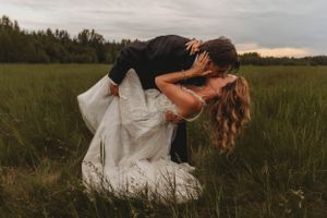 A romantic dip kiss in a rustic grass field at sunset with the bride wearing a flowing white gown.