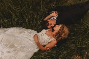 A couple laying in tall grass during a romantic wedding photoshoot at dusk.