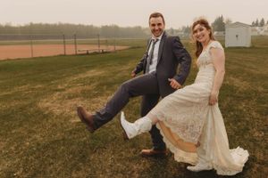 Playful wedding couple showing off dance moves on grassy field.