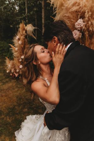A romantic wedding kiss against a backdrop of pampas grass and autumn decor.